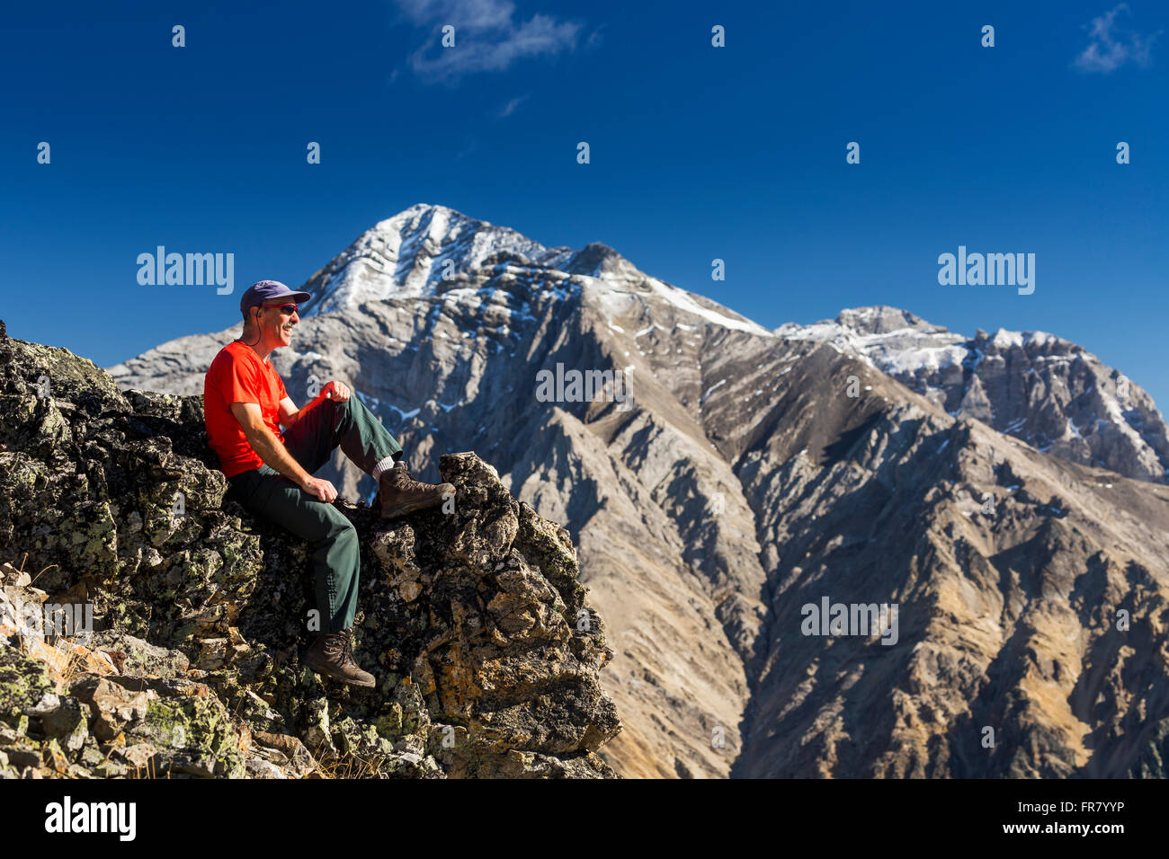 Male hiker sitting on top of mountain ridge overlooking snow peaked ...