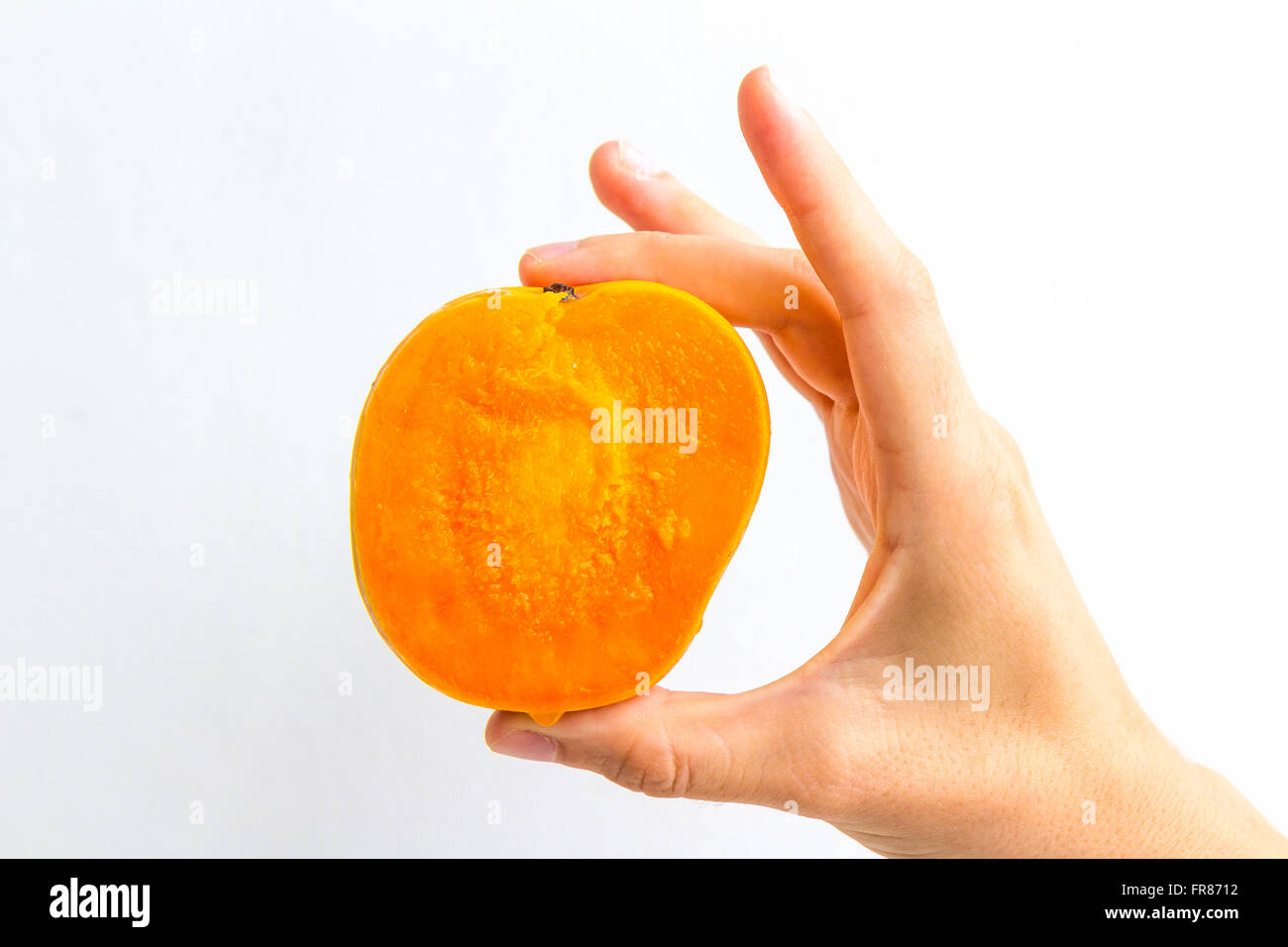 A very ripe mango, sliced in half, held in the hand of a young woman ...