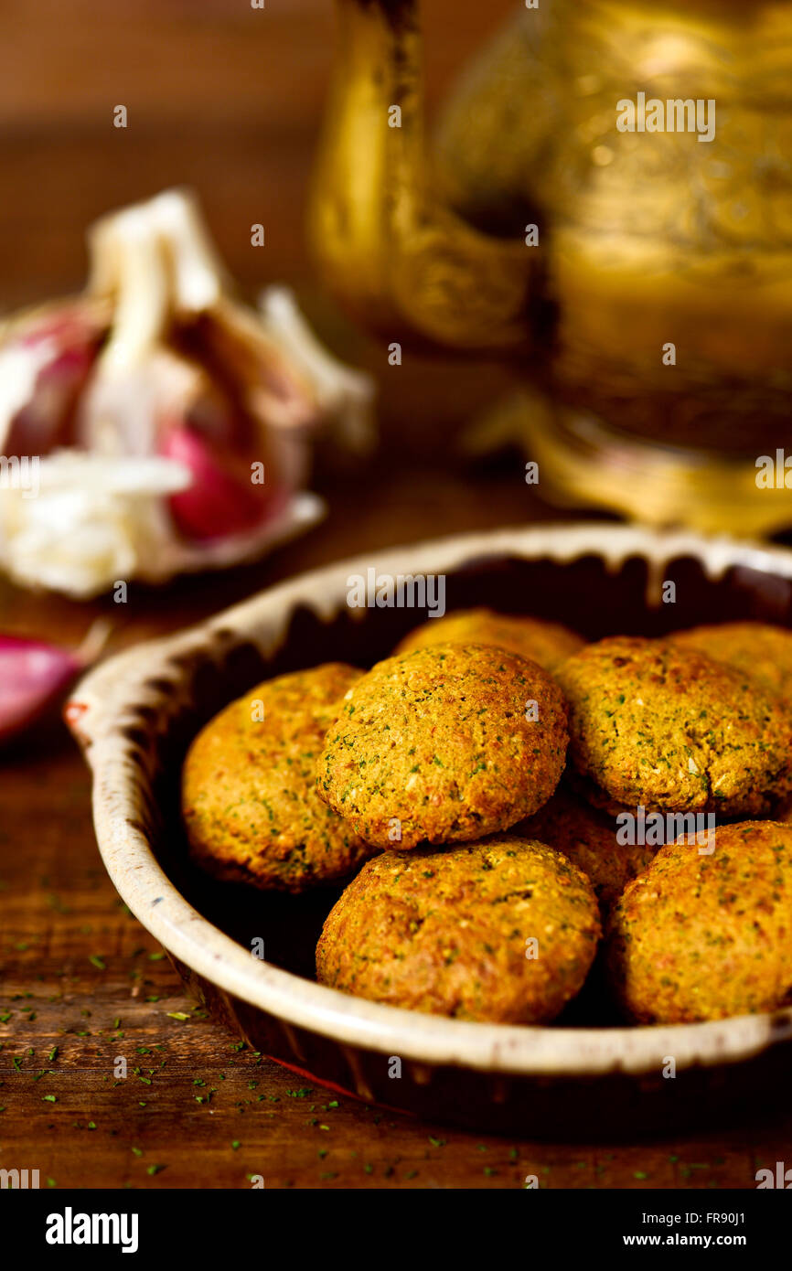 closeup of an earthenware plate with some falafel on a rustic wooden table with a golden teapot in the background Stock Photo