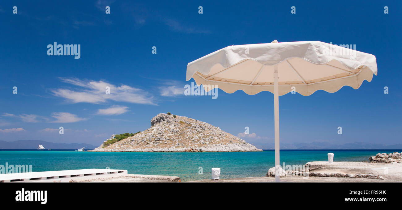Pedi, Symi, South Aegean, Greece. Panoramic view across turquoise sea to the offshore island of Agia Marina. Stock Photo