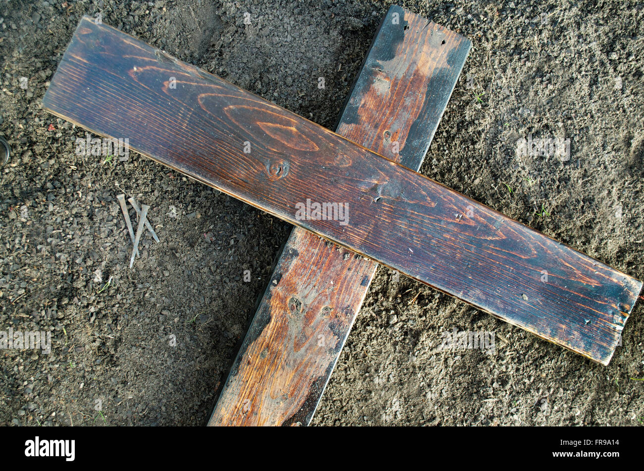 Wooden Cross laying on the ground with three nails nearby Stock Photo