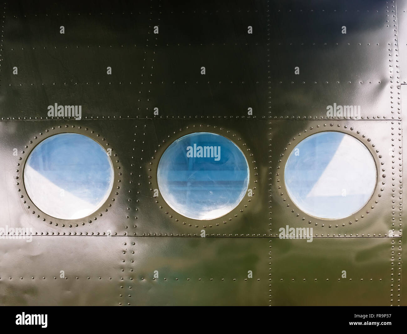 Portholes on military green painted metal background with rivet. Three portholes on board old retro airplane. Stock Photo