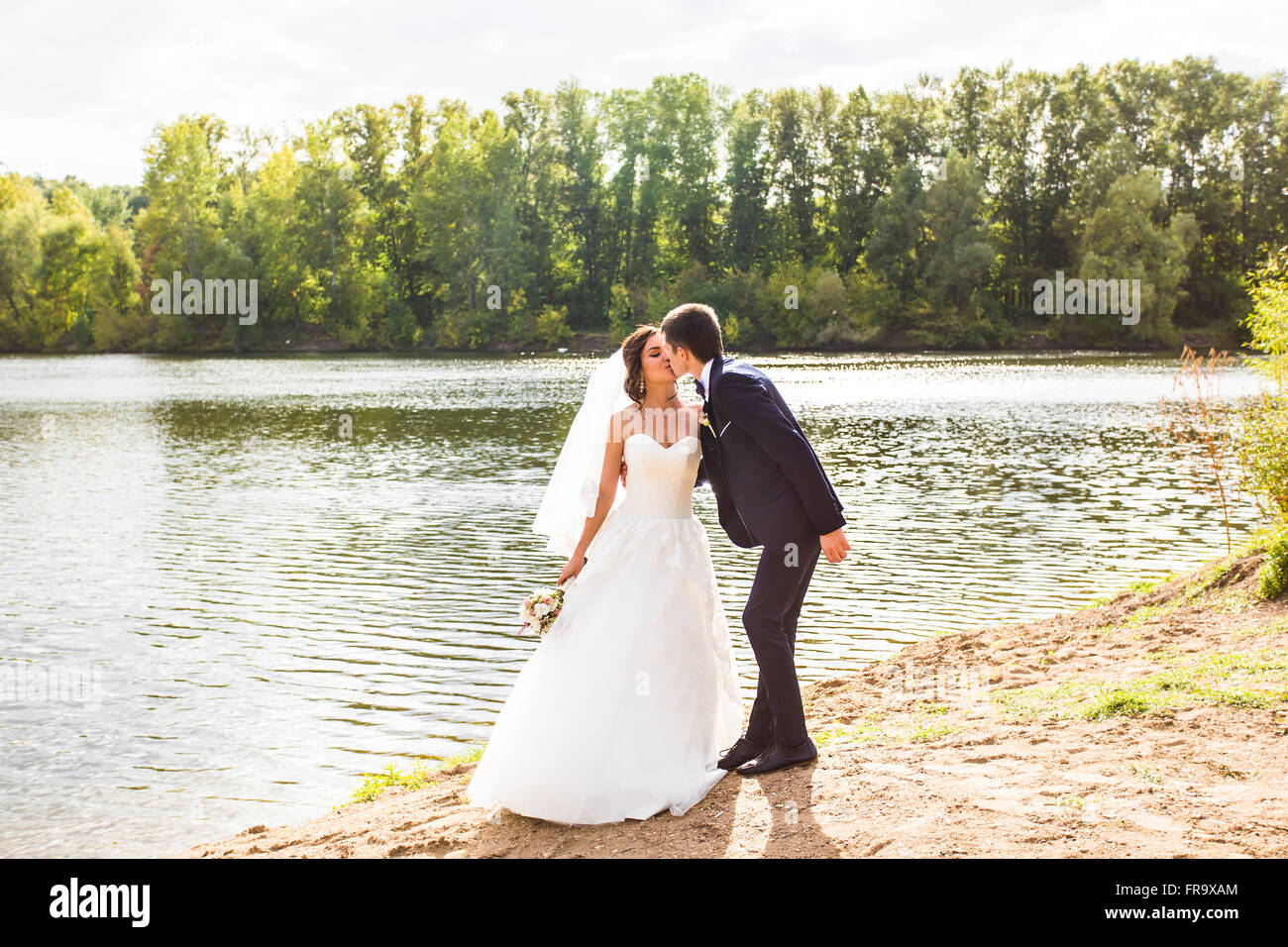 Wedding couple standing and kissing near lake Stock Photo - Alamy