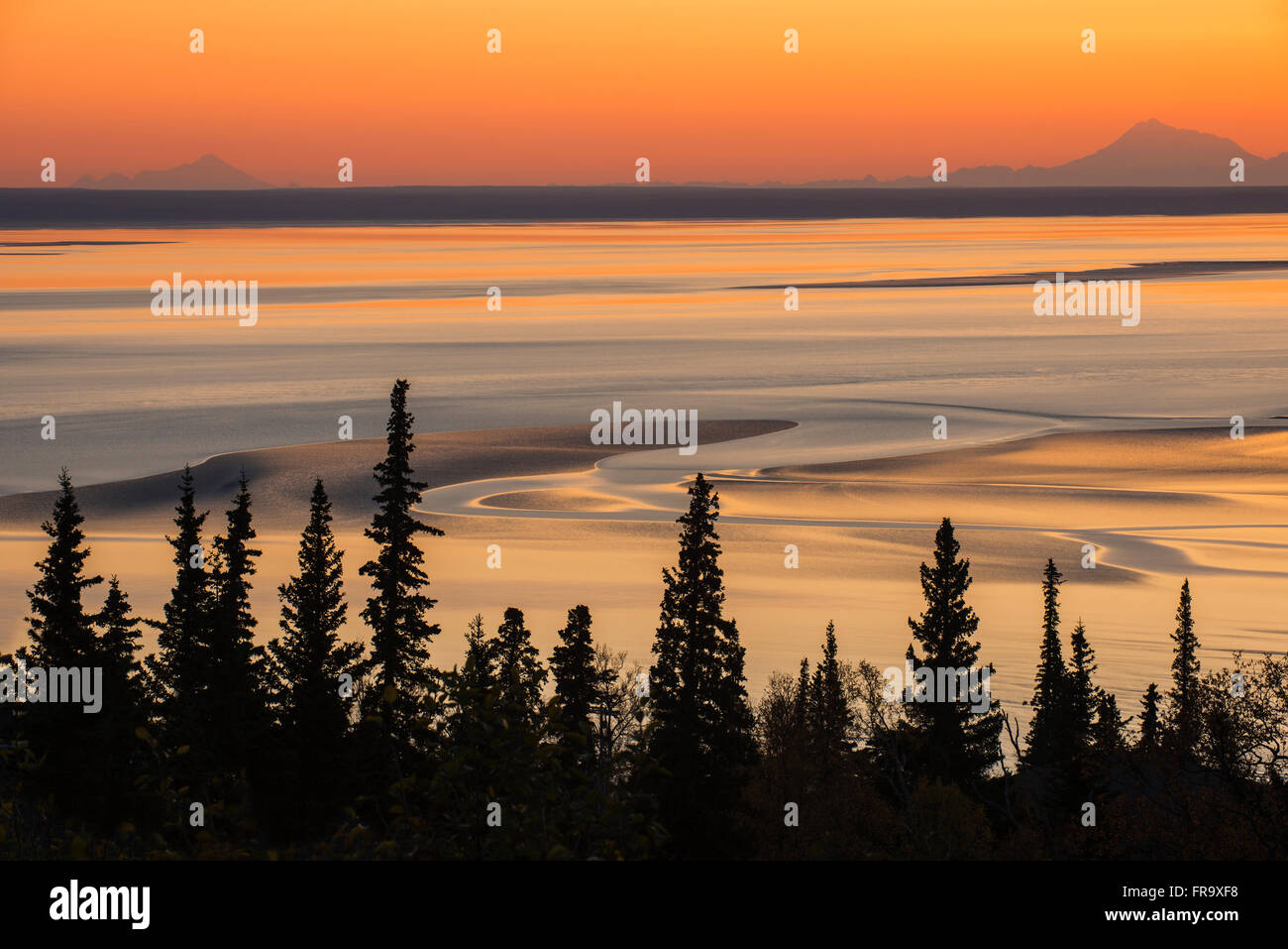 Swirling patterns in the mudflats at low tide and sunset, with Mt. Iliamna and Mt. Redoubt on the horizon, Turnagain Arm, Southcentral Alaska Stock Photo