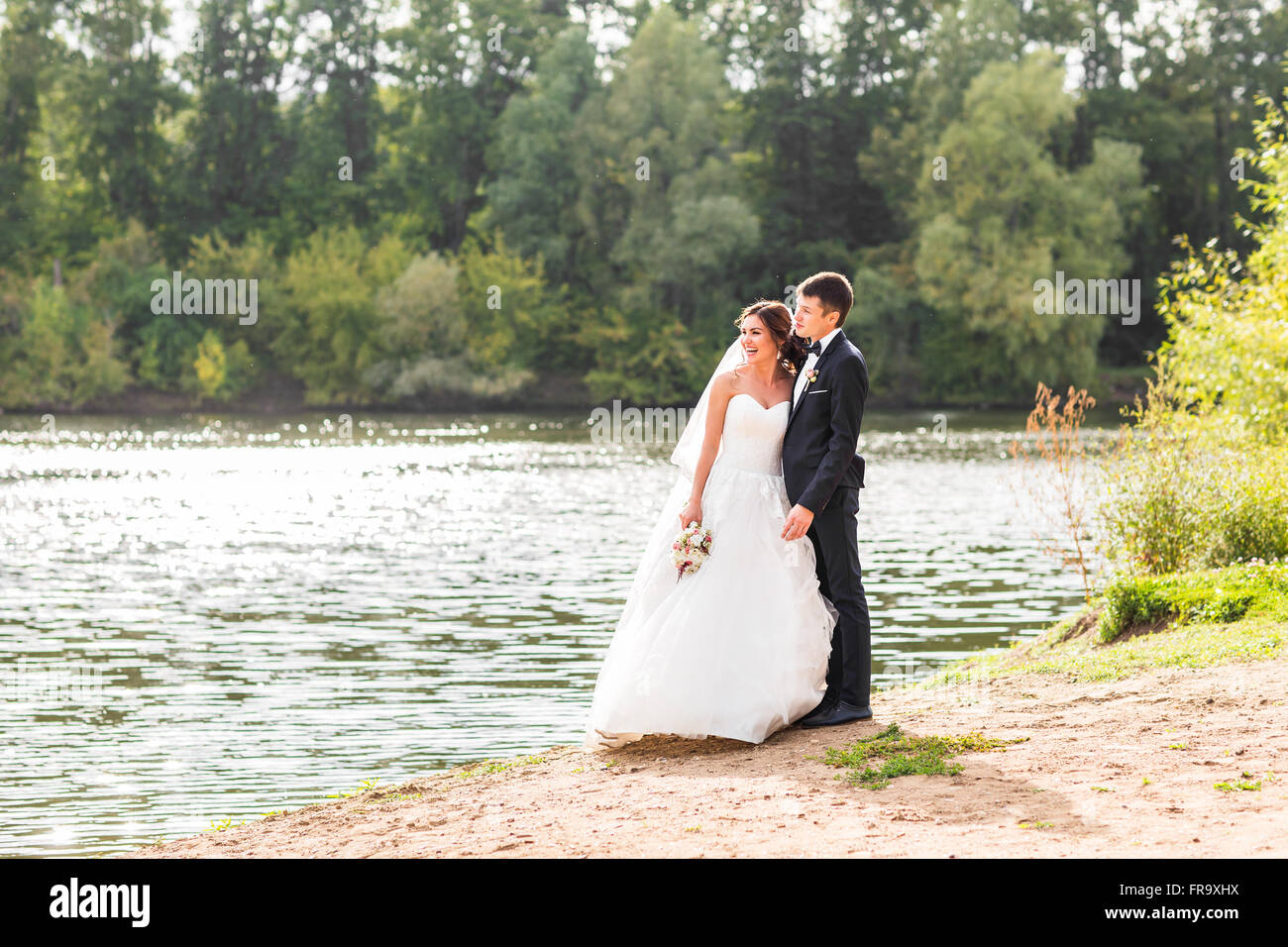 Wedding couple standing and hugging near lake Stock Photo - Alamy