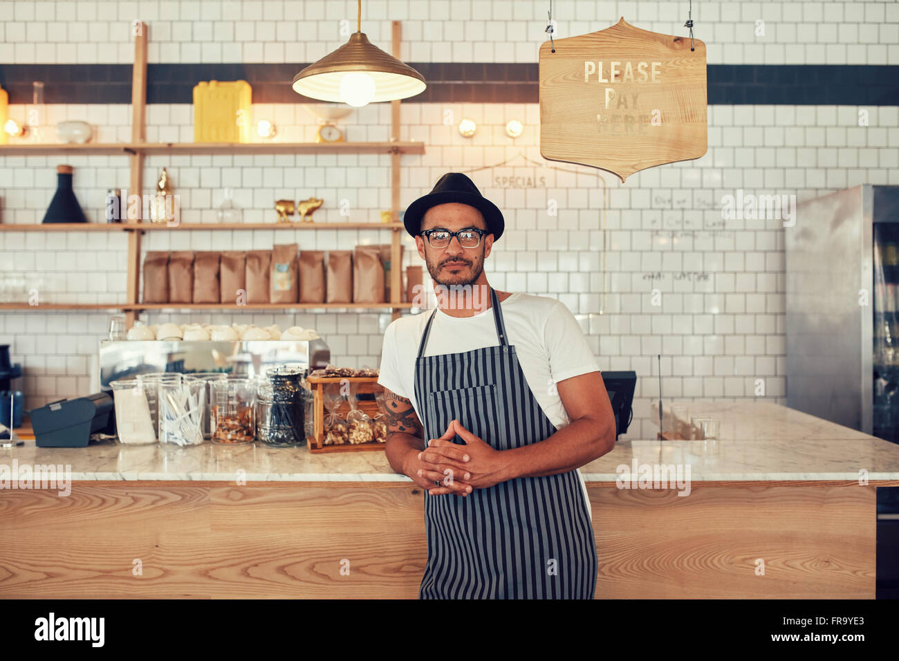 Portrait of a confident young coffee shop owner standing at the cafe counter. Handsome young man working at a restaurant and wea Stock Photo