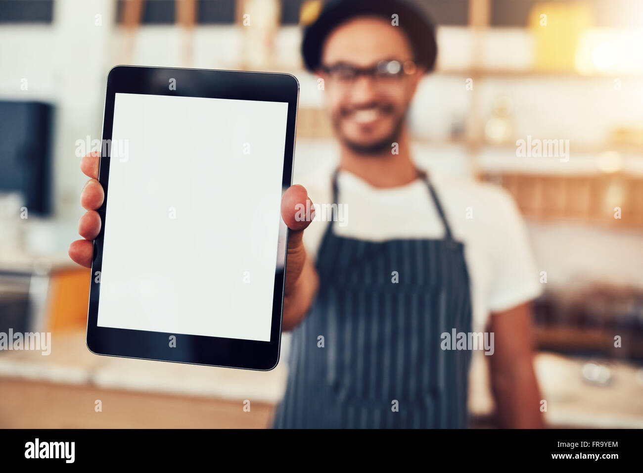 Close up portrait of a waiter holding up a tablet computer with a empty display. Coffee shop owner showing a digital tablet. Stock Photo