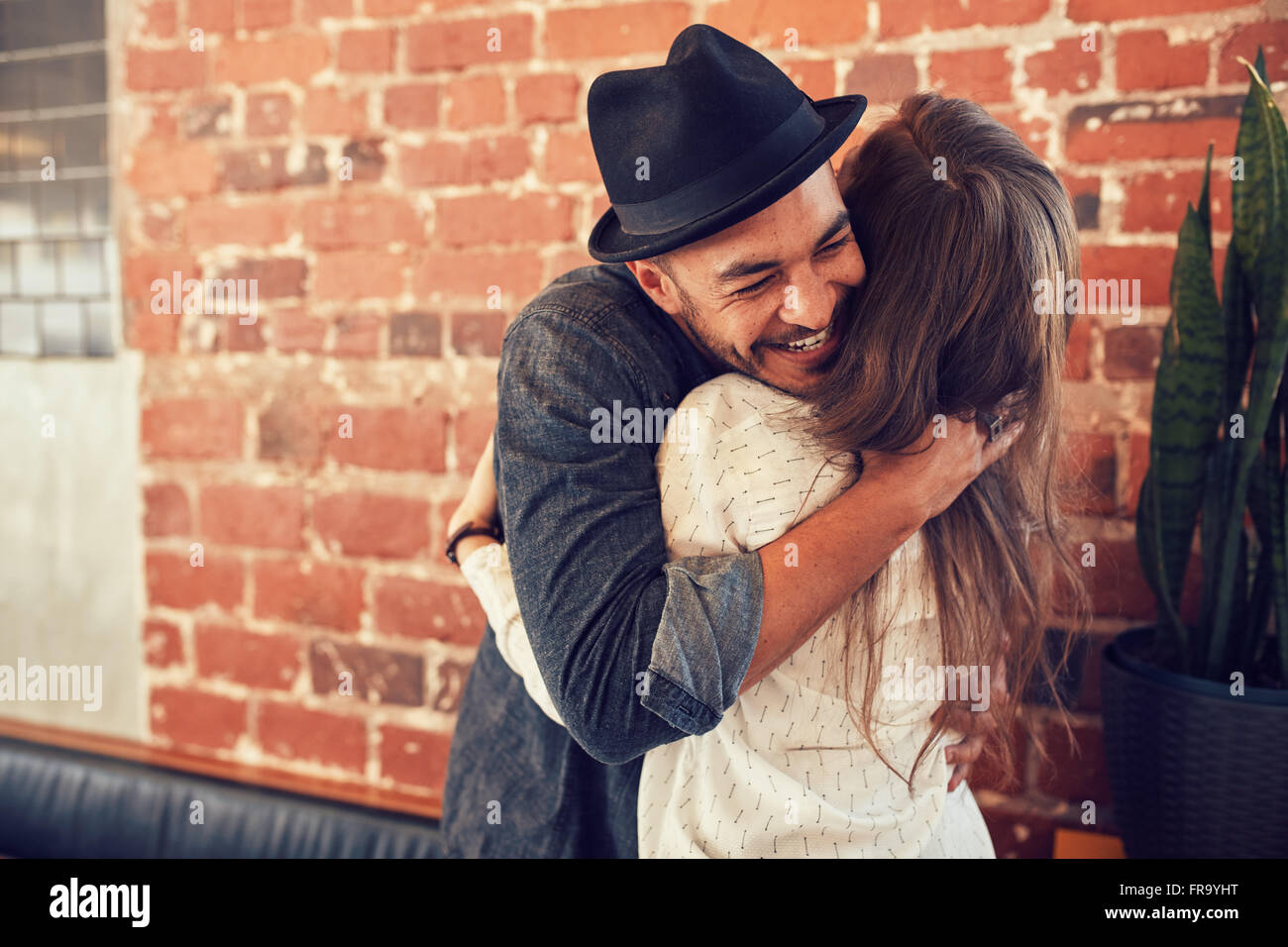 Portrait of young man embracing his girlfriend at cafe. Young man hugging a woman in a coffee shop. Stock Photo