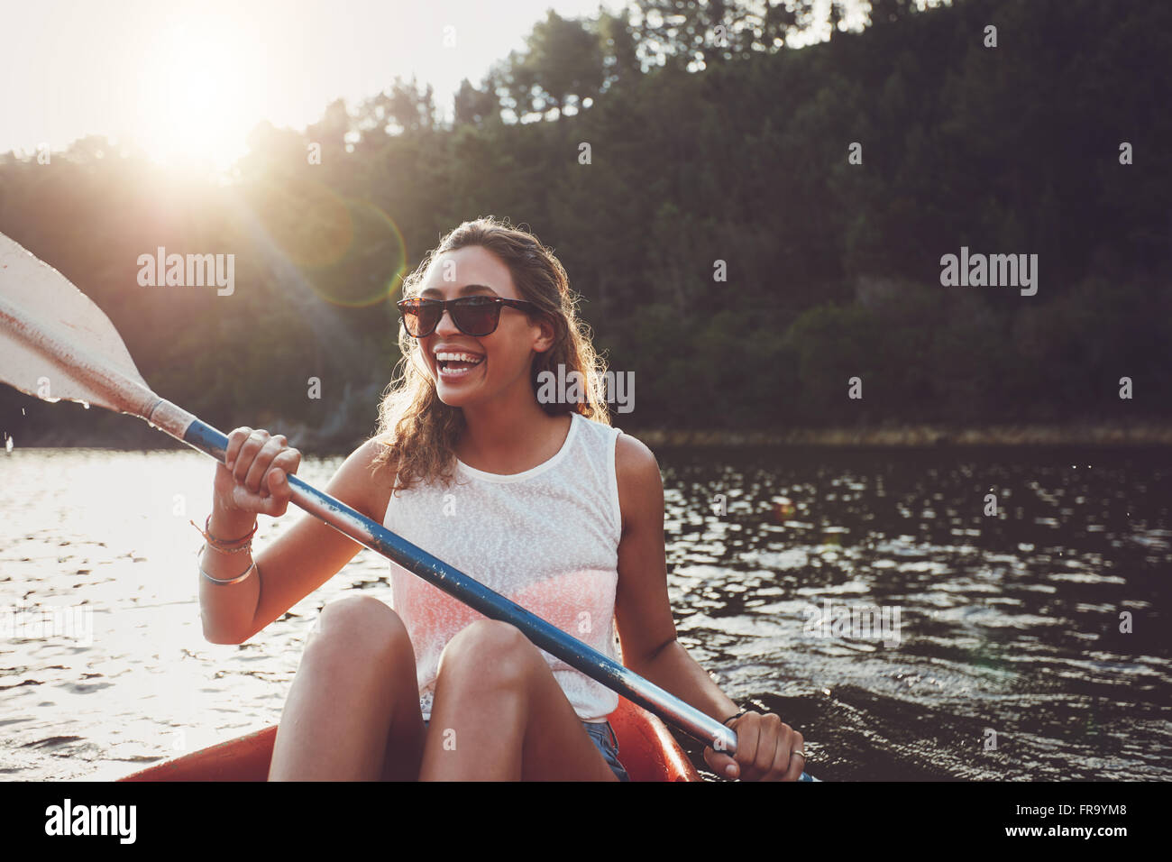 Smiling young woman kayaking on a lake. Happy young woman canoeing in a lake on a summer day. Stock Photo