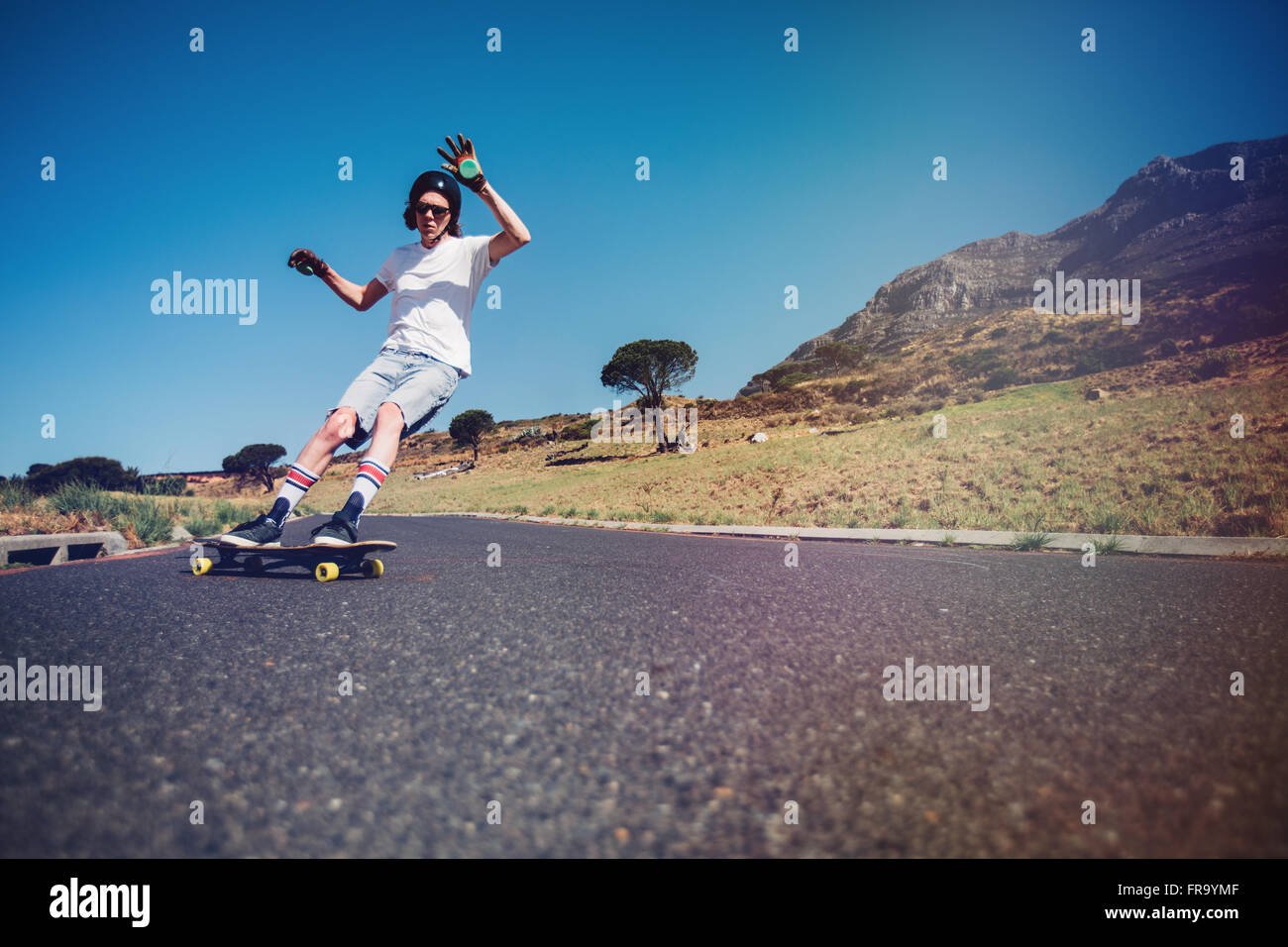 Young man longboarding on a road. Young guy wearing protective gear