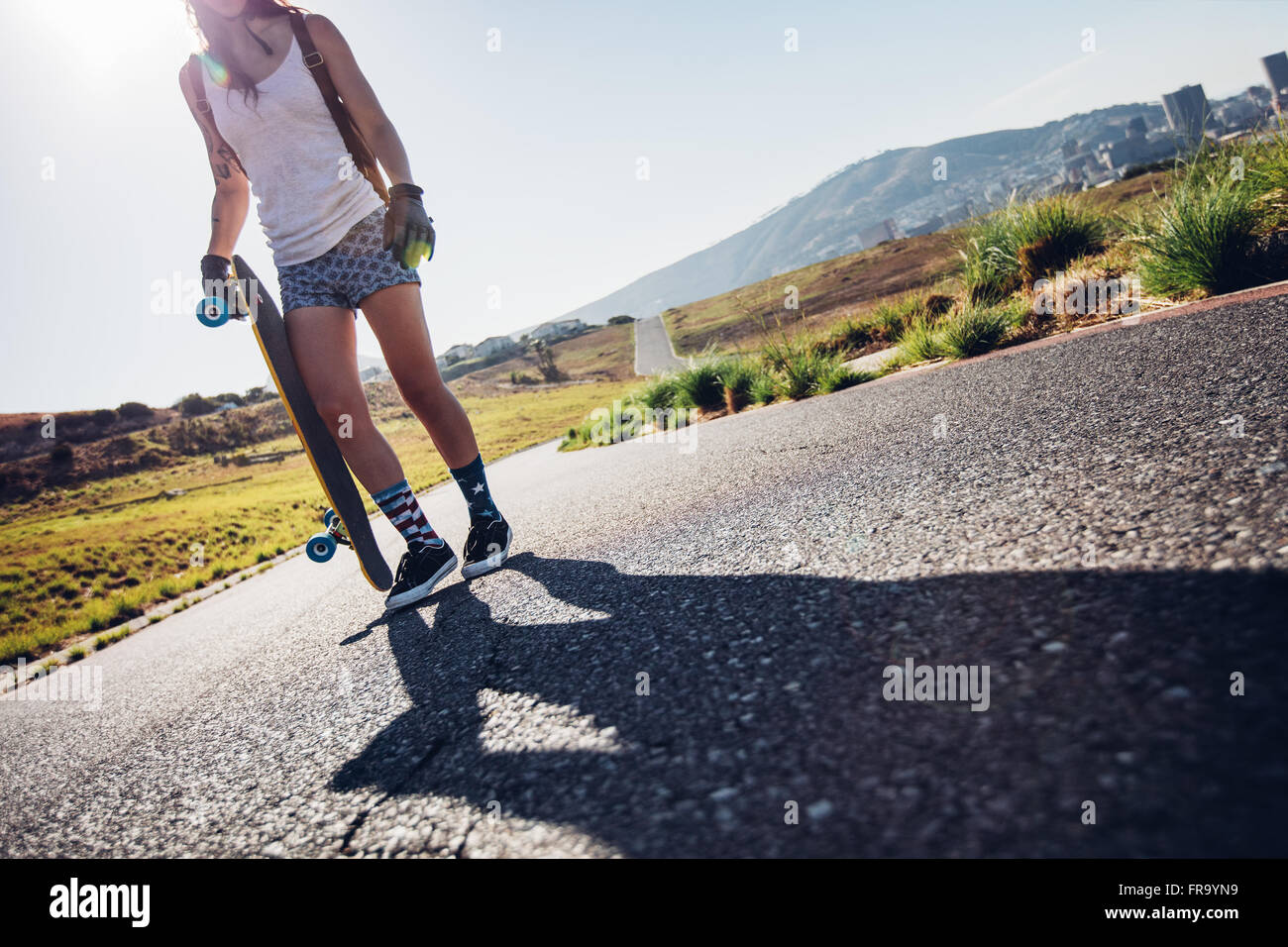 Cropped shot of young woman walking with her skateboard on road. Young female with a longboard on a sunny day. Stock Photo