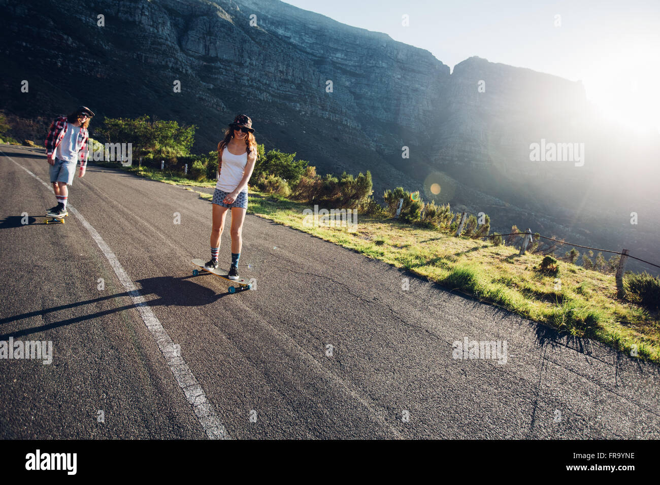 Two young people skating outdoors on rural road. Man and woman longboarding on a summer day. Stock Photo