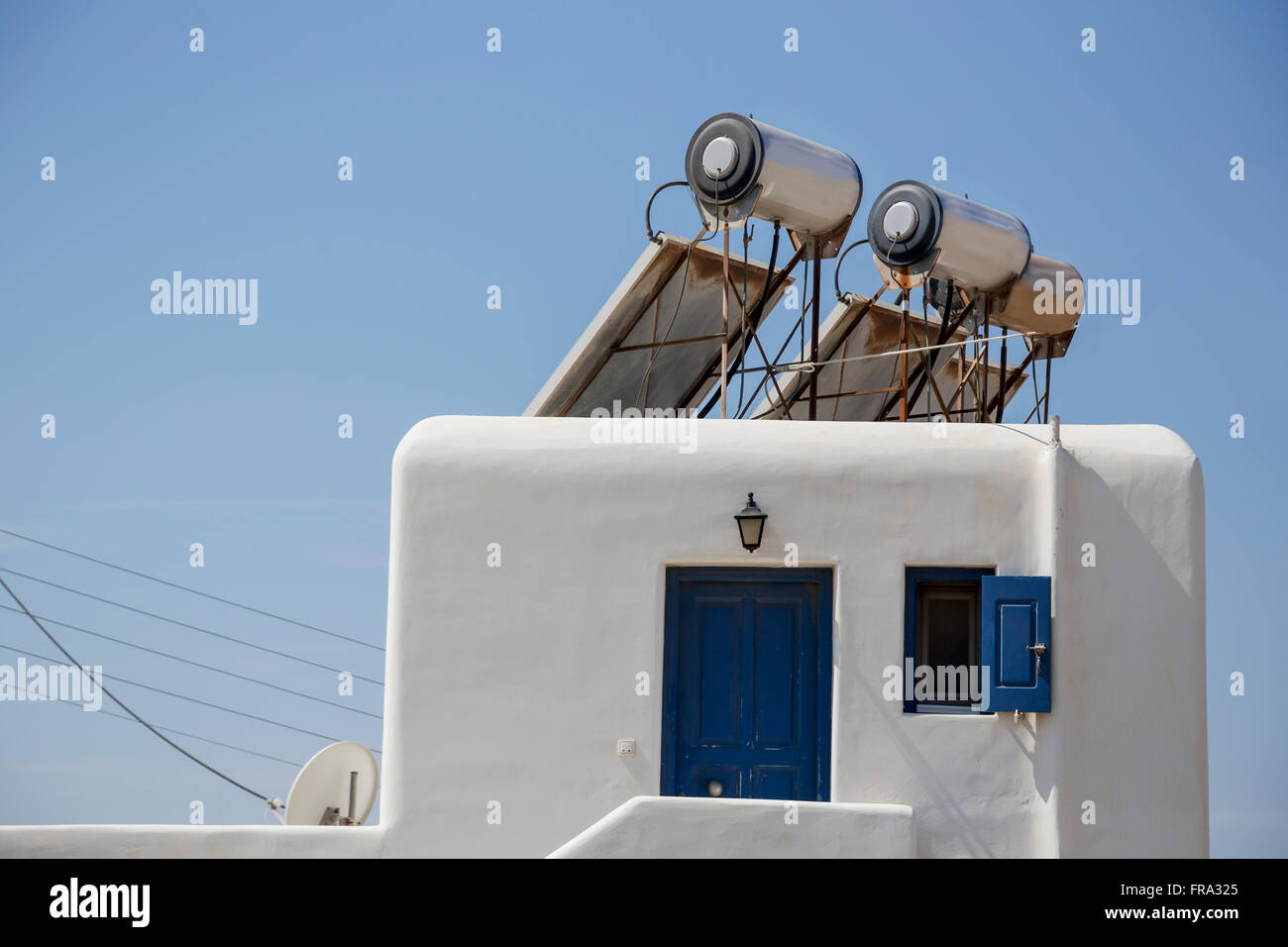 Modern solar panel powered hot water heaters for energy efficiency are mounted on the roof of a traditional greek home; Mykonos, Greece Stock Photo