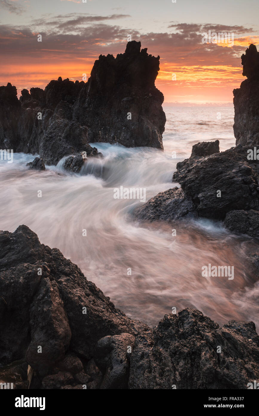 Surf comes in through rocks at sunrise; Laupahoehoe, Island of Hawaii, Hawaii, United States of America Stock Photo