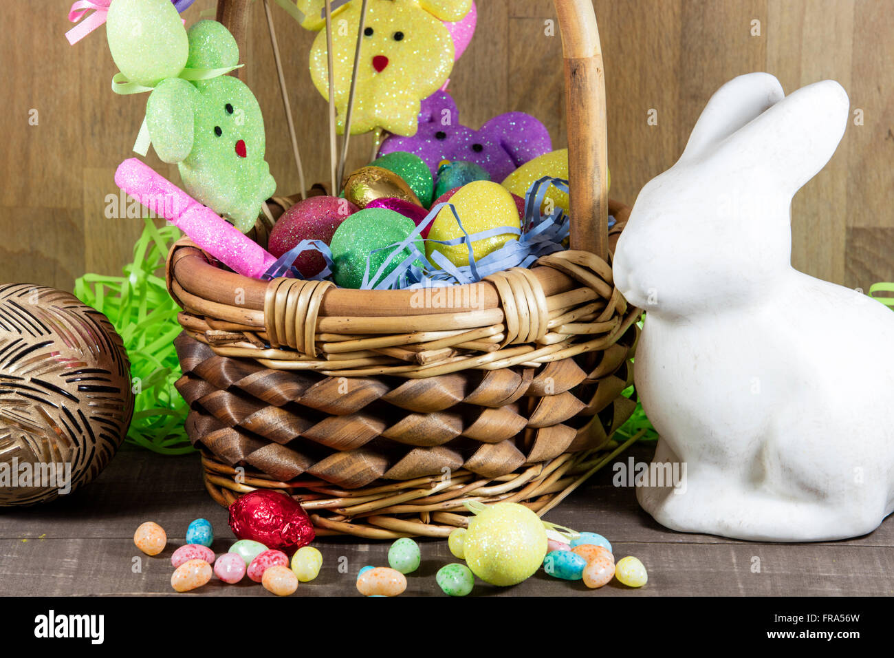 Easter basket filled with colored eggs and bunnies, with candy on table top Stock Photo