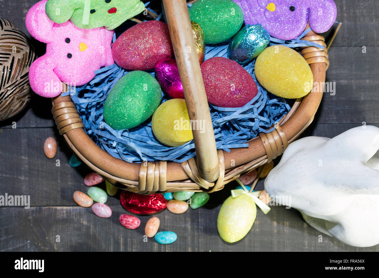 Easter basket filled with colored eggs and bunnies, with candy on table top Stock Photo