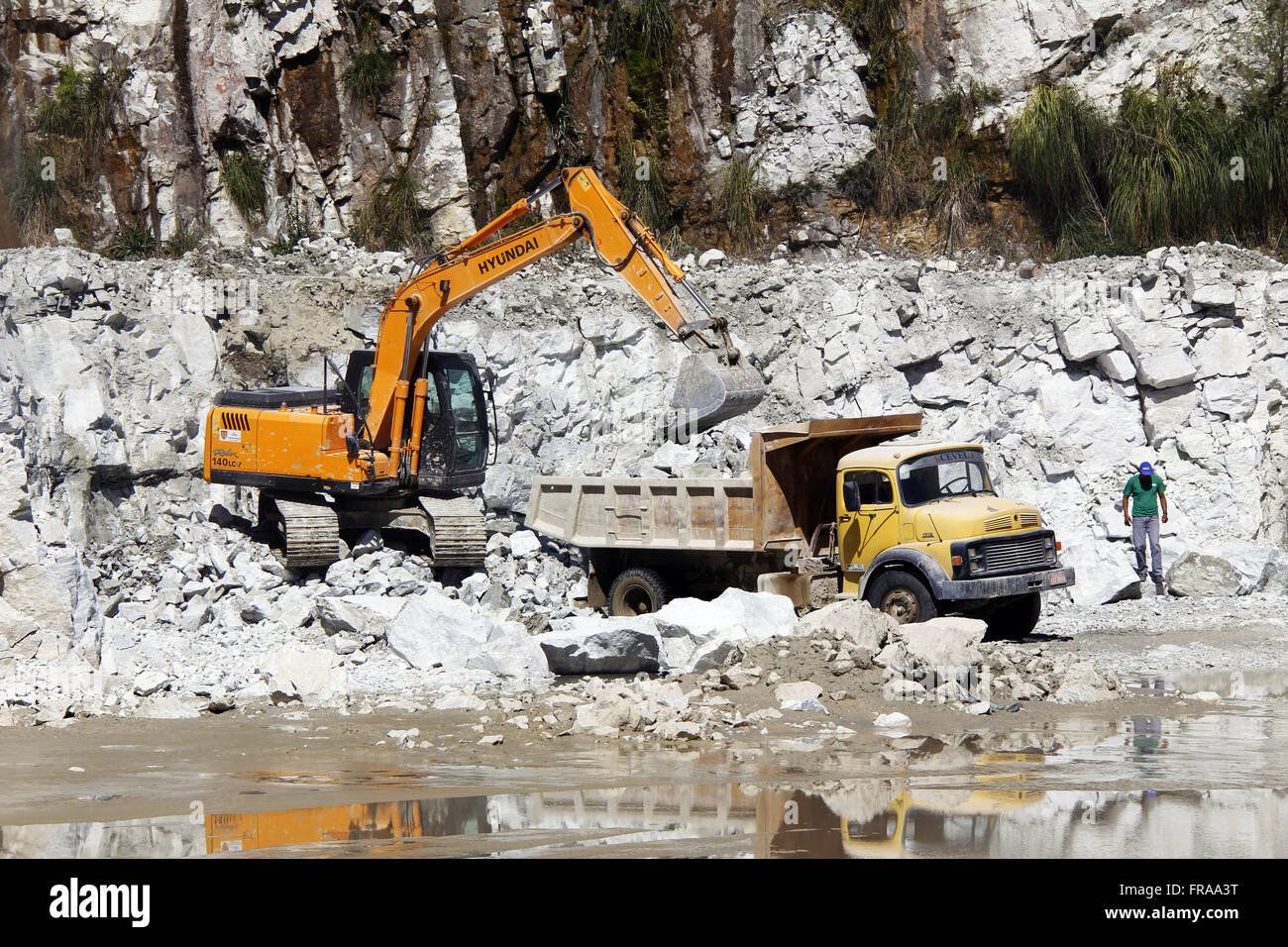 Backhoe loading truck in limestone rocks after explosion at the open pit Stock Photo