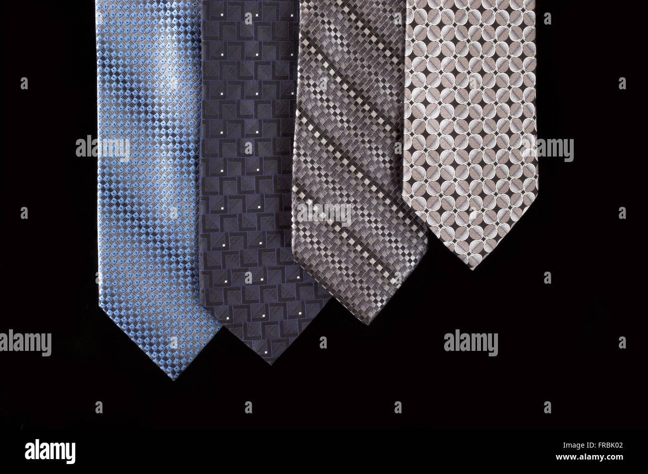 four neckties hanging vertically and isolated against black background Stock Photo
