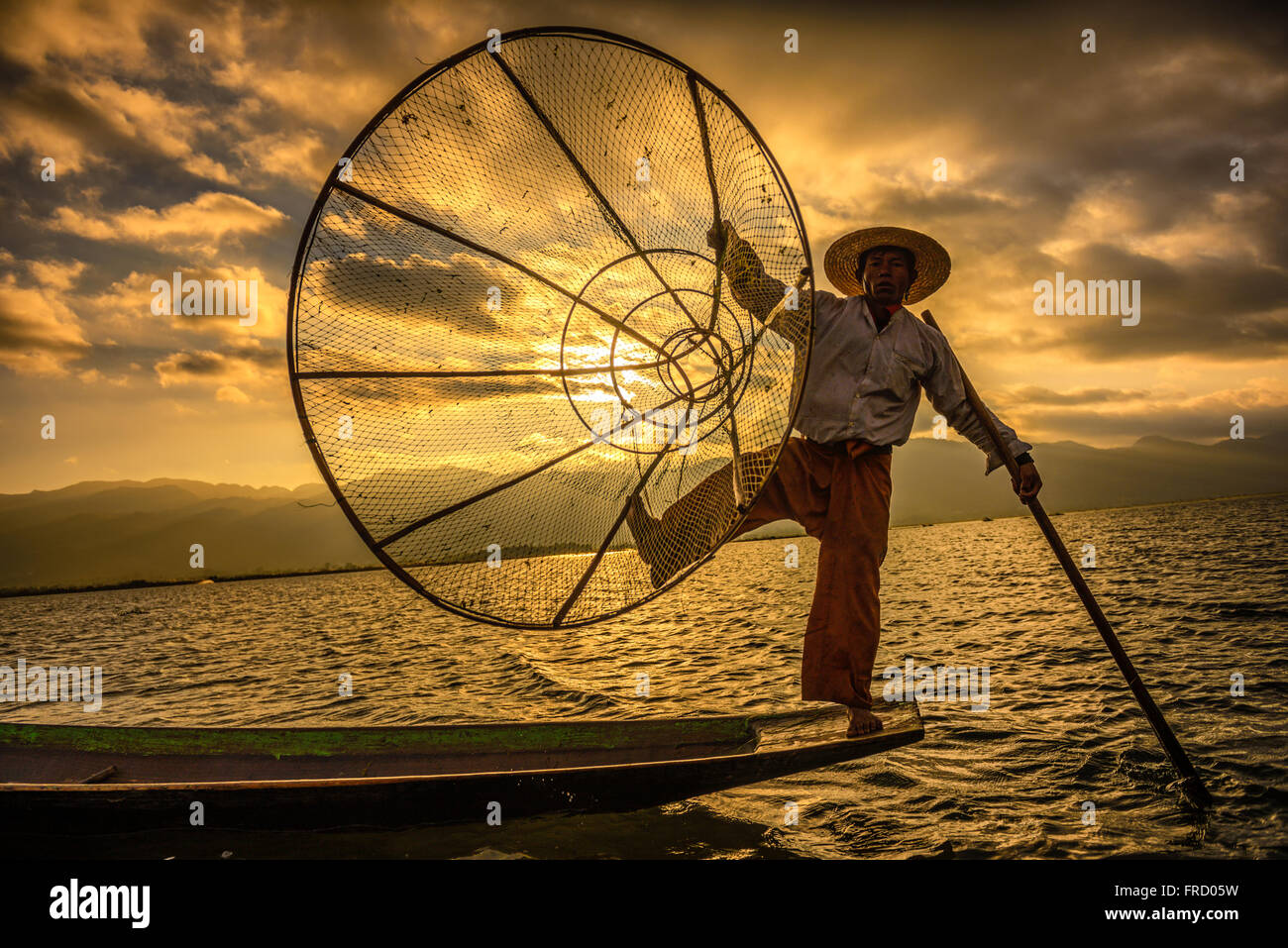 Burmese fisherman fishing on a traditional bamboo boat with a handmade net at sunrise Stock Photo