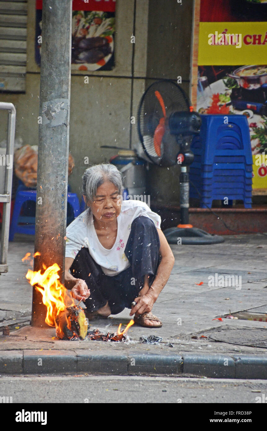 Old woman cooking on a fire beside a street in Hanoi, Vietnam Stock Photo