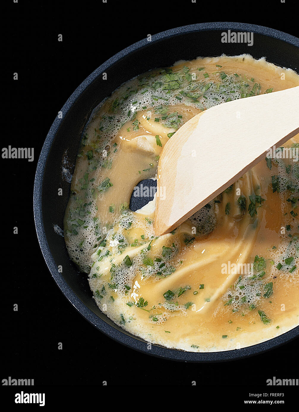 Classic french omelette: 4, a wooden spatula pulling cooked egg towards the centre of the pan. Stock Photo