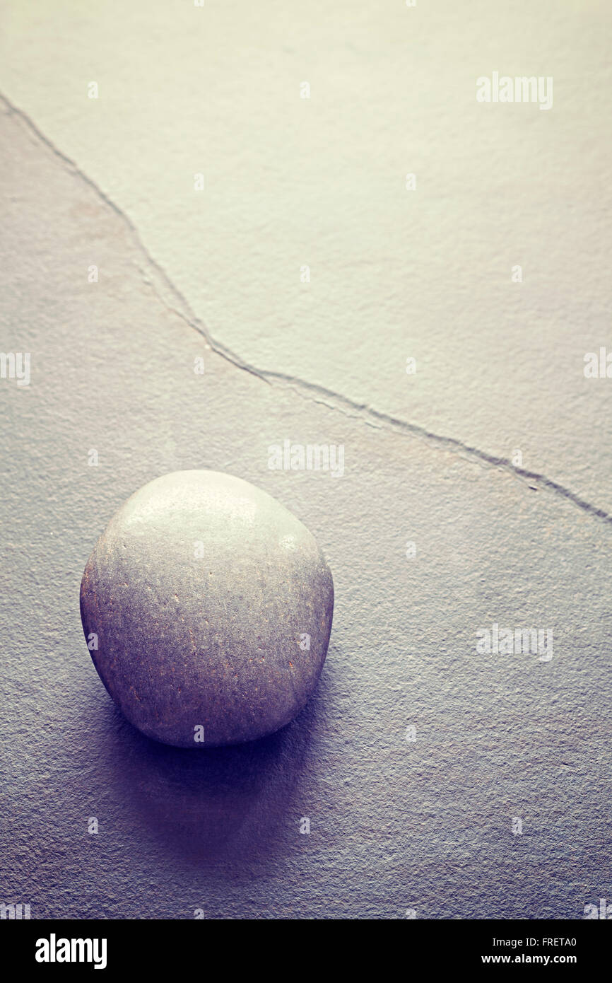 Vintage toned rounded stone on a slate, abstract natural background with copy space. Stock Photo