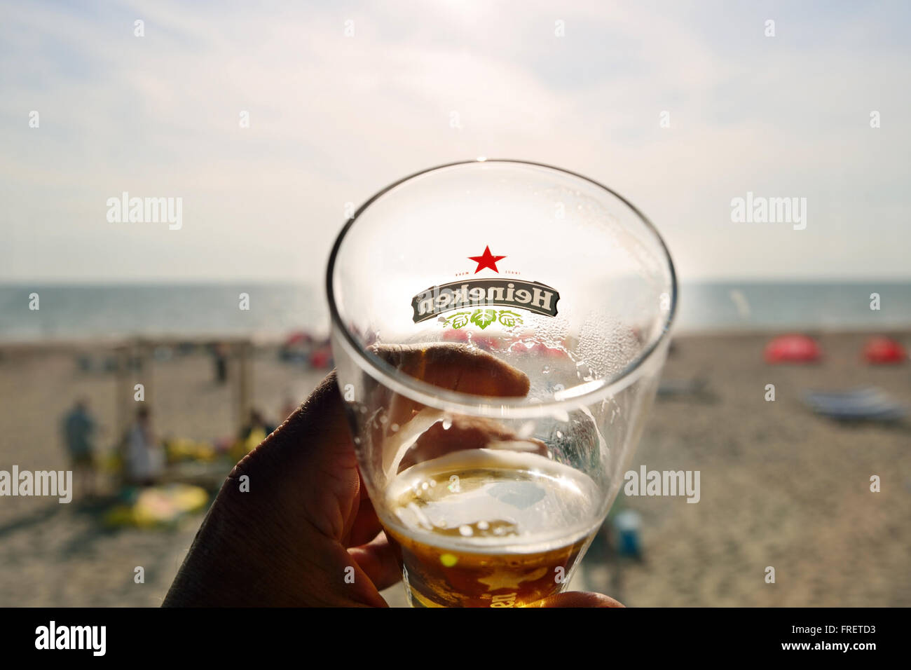 Hand holding a Glass of Heineken beer when the sun sets on the beach. Stock Photo