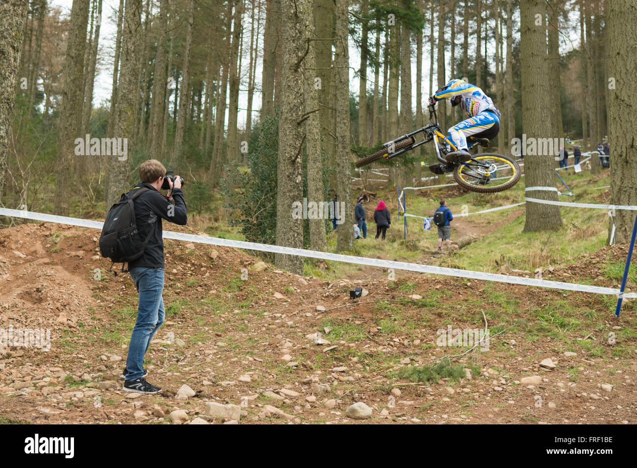 photographer capturing the action as Elliott Heap clears a jump at the 2016 SDA downhill mountain bike race at Ae forest Scotland Stock Photo