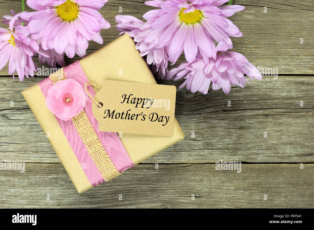 Gift box with Happy Mothers Day tag on rustic wood background with soft purple daisies Stock Photo