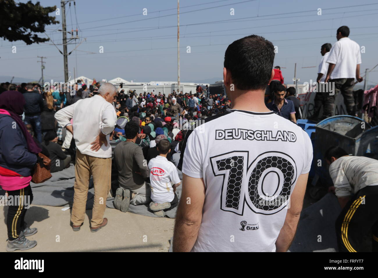 Idomeni, Greece, 22 March 2016. A man wearing a Germany national football team replica t-shirt looks at a 'Open the Borders' sit-in protest at railway tracks at a makeshift camp for refugees and migrants at the Greek-Macedonian border, near the village of Idomeni. Credit:  Orhan Tsolak / Alamy Live News Stock Photo