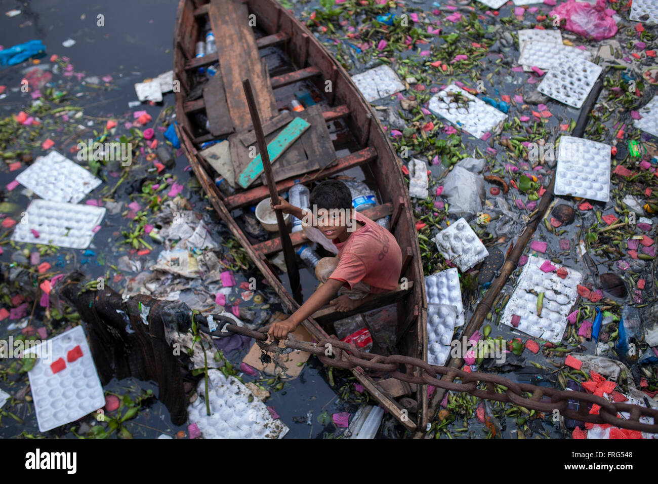 Dhaka, Bangladesh. 21st March, 2016. A street  boy ride on a boat to collectwasteplastic bottle at the Buriganga river which is full of pitch- black colour water in Dhaka, Bangladesh on March 21, 2016. A large swathe of the Buriganga River which is the lifeline of the capital has turned pitch-black with toxic waste, oil and chemicals flowing into it from industrial units.  Buriganga river, which flows by Dhaka is now one of the most polluted and biologically dead rivers in Bangladesh. Credit:  zakir hossain chowdhury zakir/Alamy Live News Stock Photo