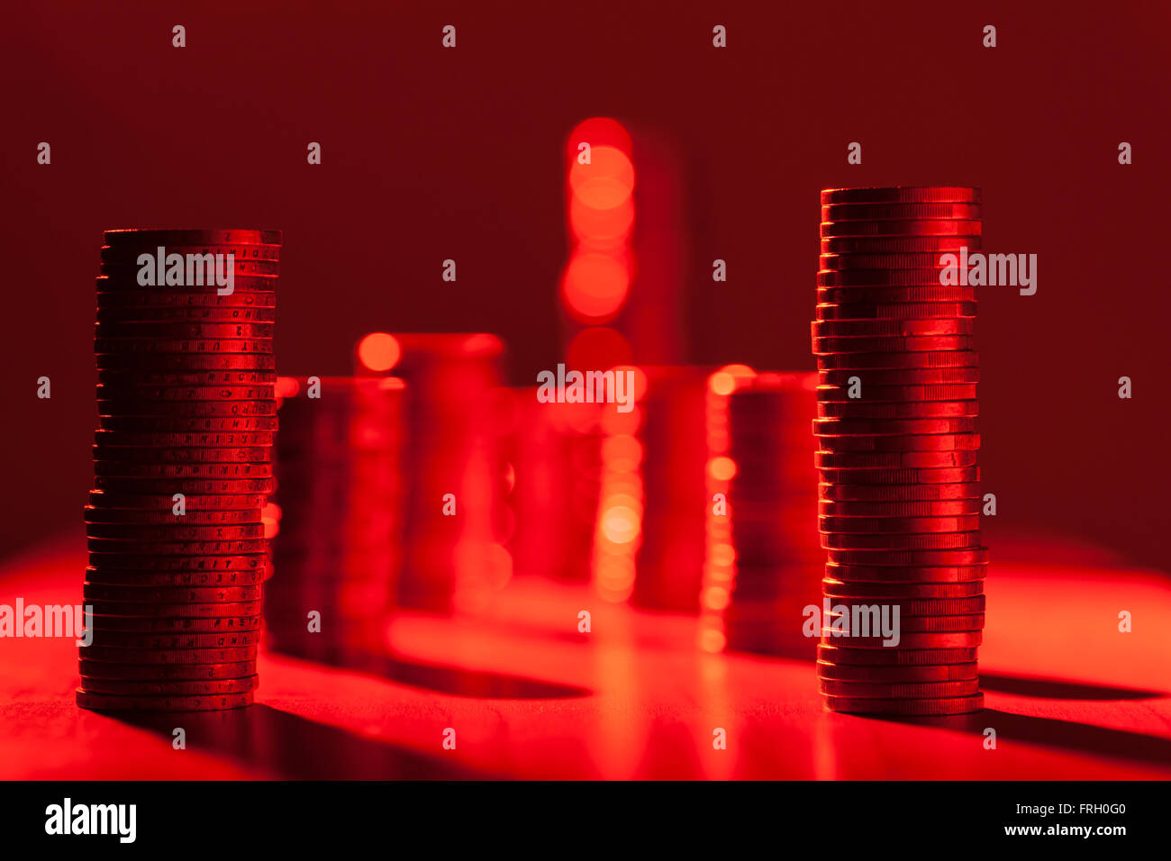 flat angled view of side by side stacked coins in the red light at aperture of F5, 6; Focus on the first row Stock Photo