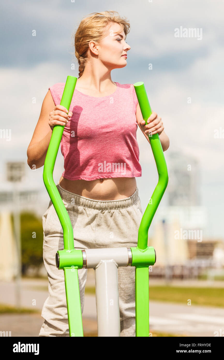Active young woman exercising on elliptical trainer machine. Fit sporty girl in training suit working out at outdoor gym. Sport Stock Photo