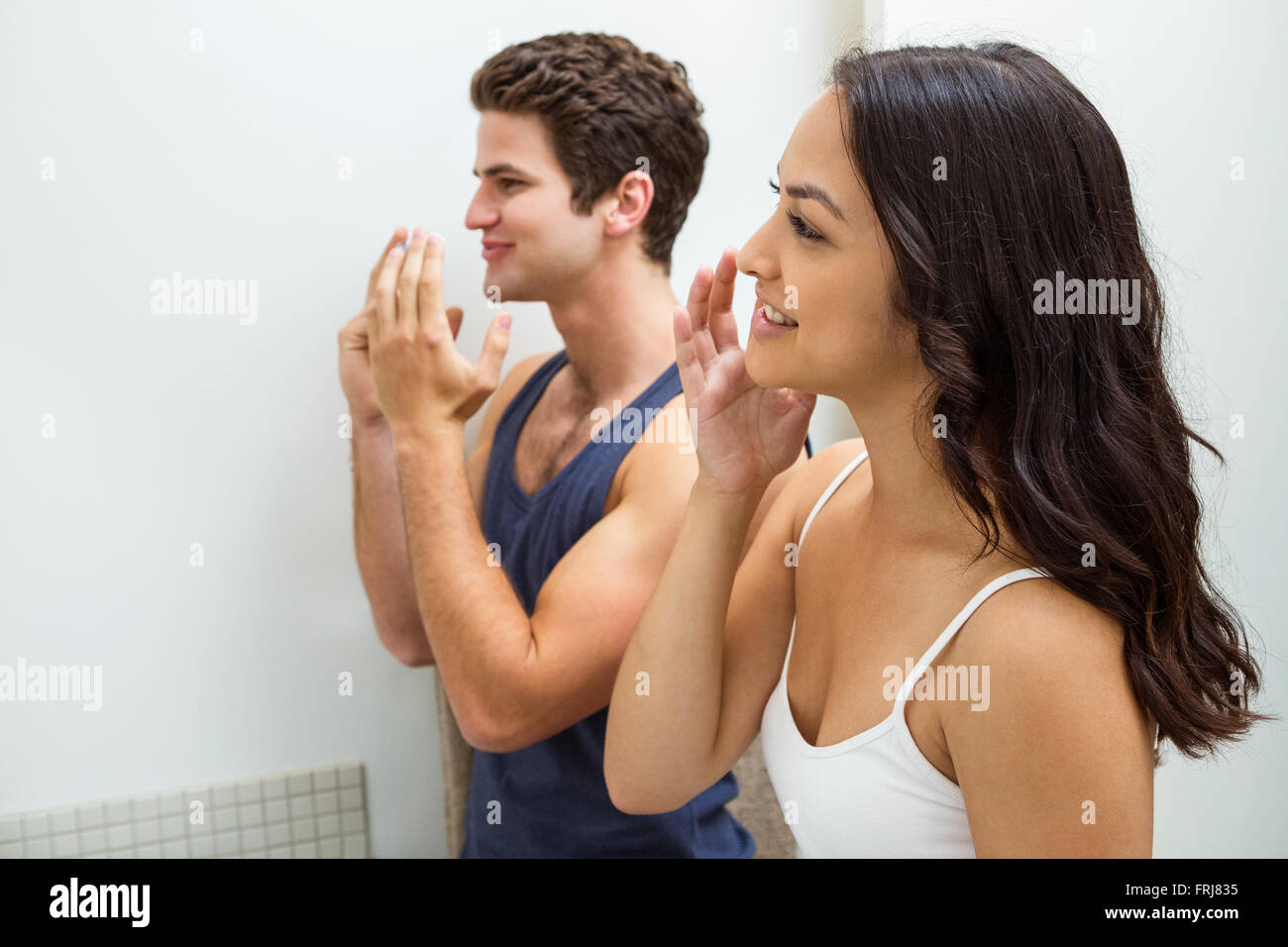 Young couple applying cream on face while looking in mirror Stock Photo