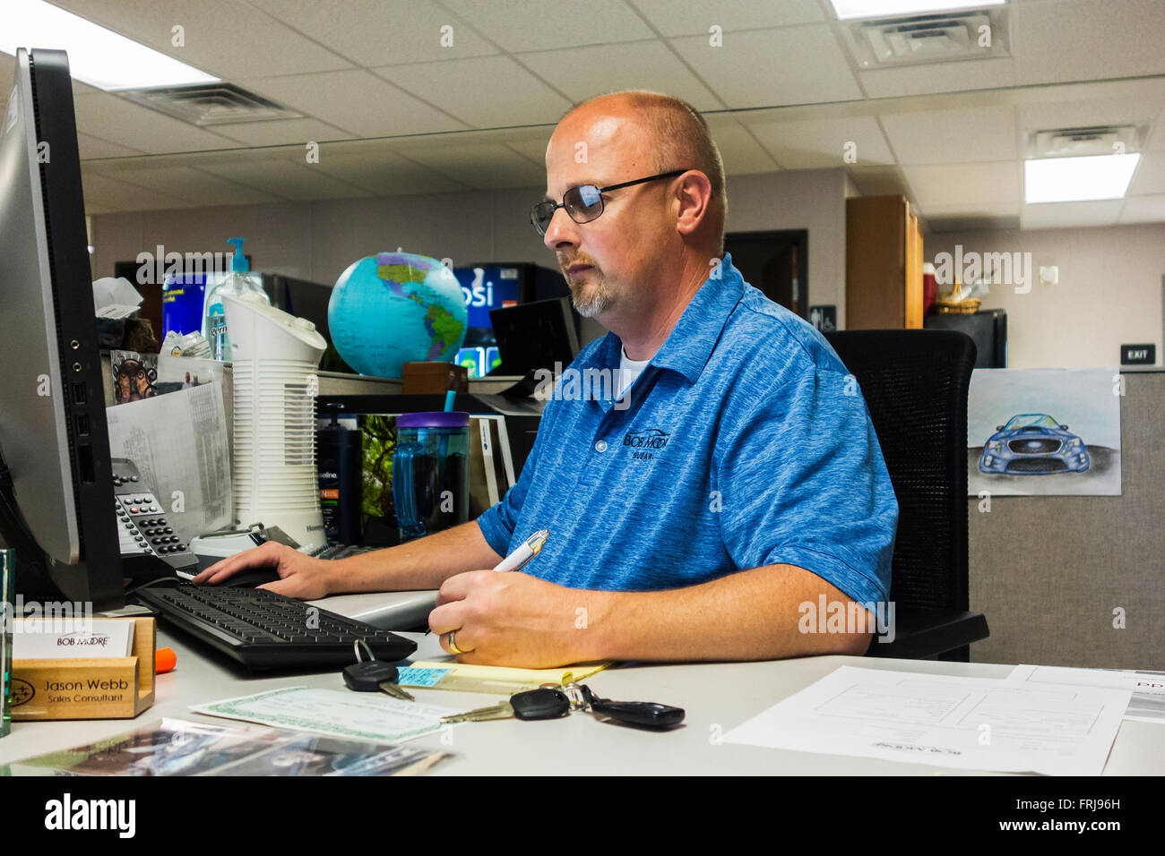 A new car salesman does the paperwork at a desk to complete a automobile purchase in Edmund, Oklahoma, USA. Stock Photo