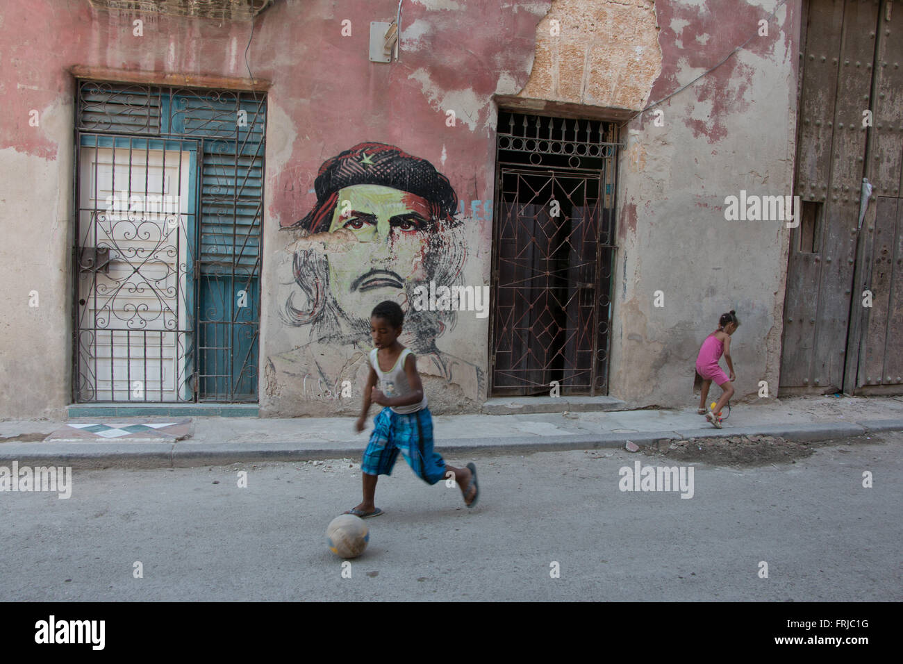 Kids playing in Old Havana in front of a faded Che Guevara painting Stock Photo