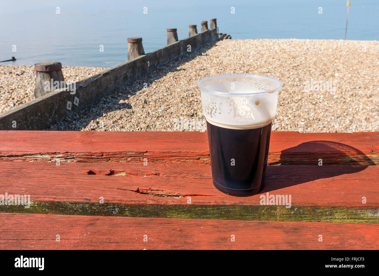 Pint of Whitstable Oyster Stout Beer on the Beach with Sunshine, Blue Sky and  Calm Sea on an early Spring Day Stock Photo