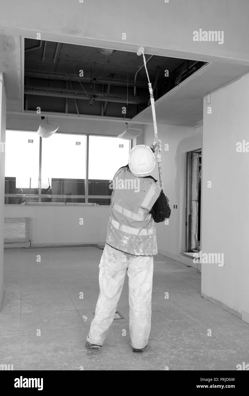 Commercial decorator at work painting a high ceiling with an extended paint roller Stock Photo