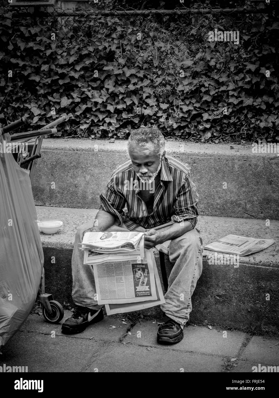 Man sat on bench outdoors reading newspaper, New York City, USA. Stock Photo