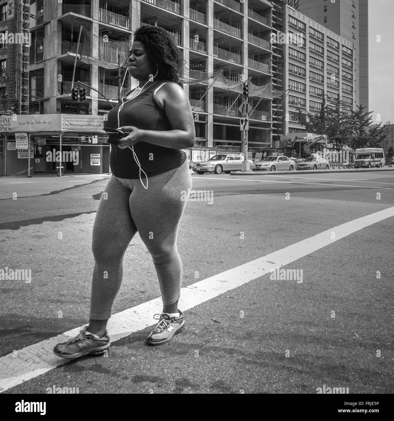 Afro-American female dressed in sportswear listening to music on her smartphone whilst exercise walking in New York City. Stock Photo