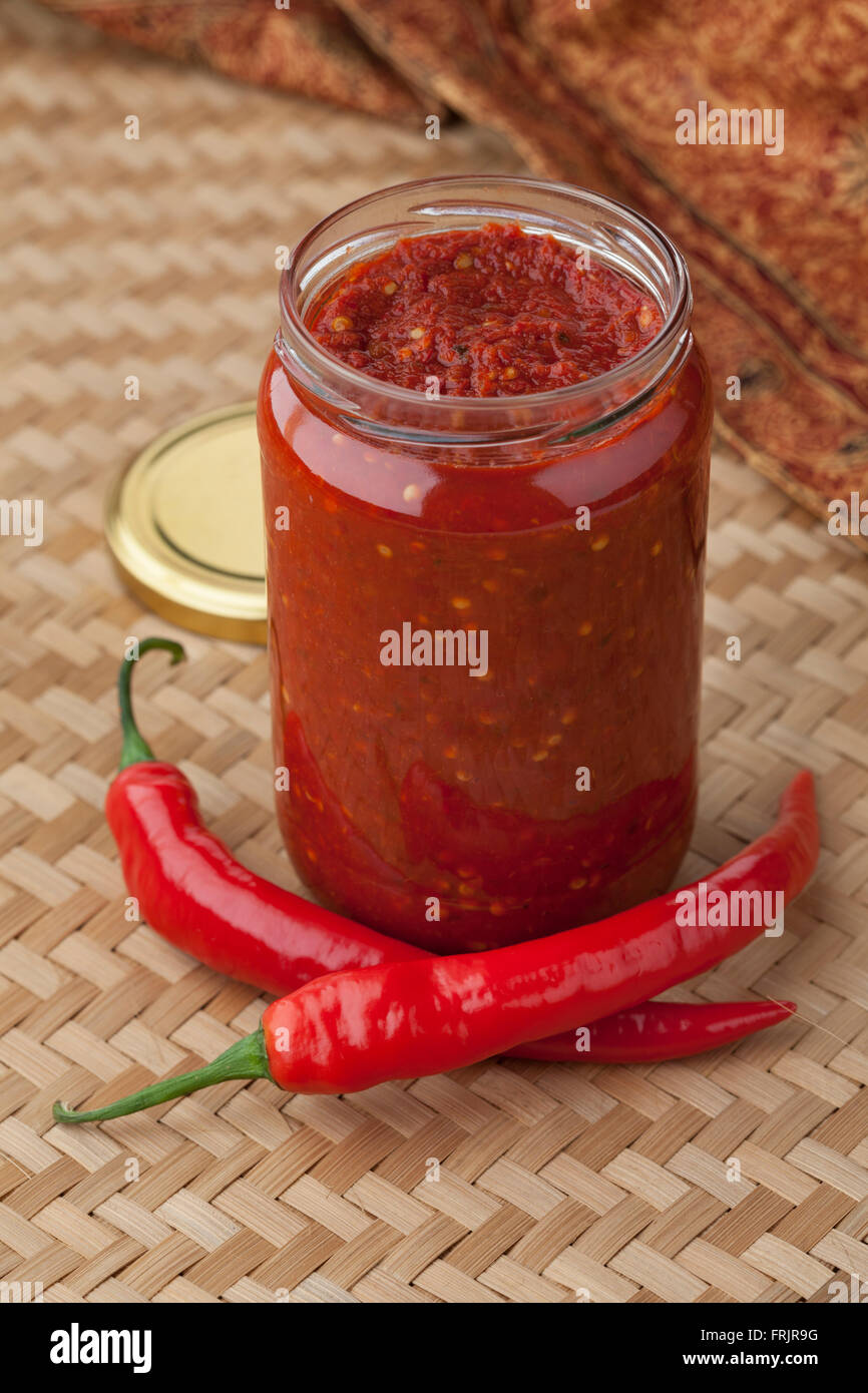 Glass jar with traditional Indonesian Sambal and fresh red chili peppers Stock Photo