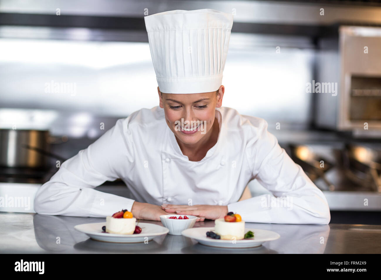Female chef looking at food plates in kitchen Stock Photo