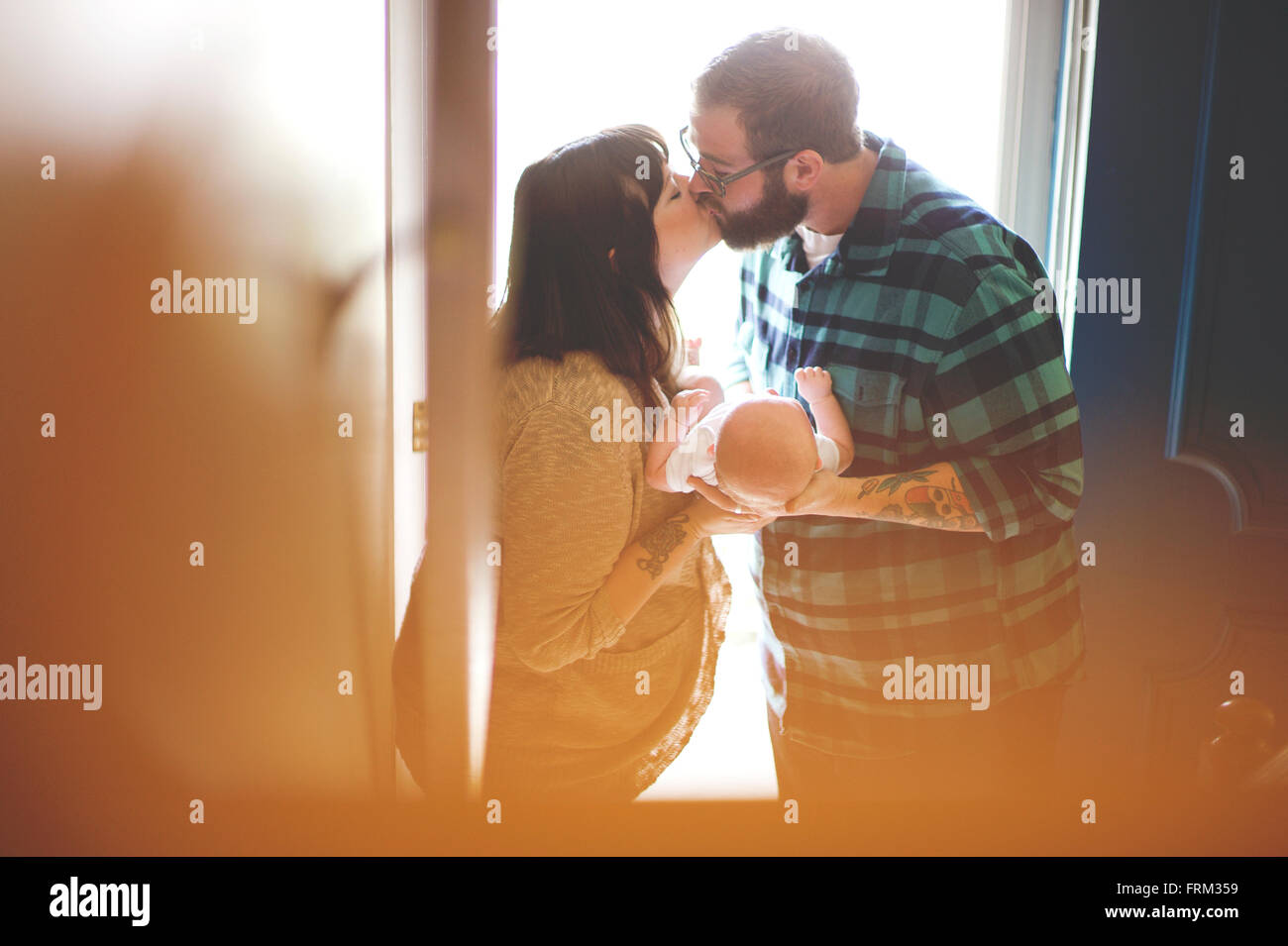 Husband and wife kiss while holding new baby Stock Photo