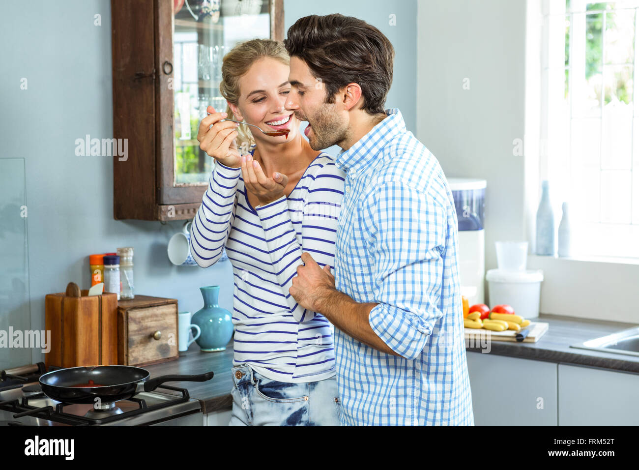 Smiling woman letting man taste a sauce with a wooden spoon Stock Photo