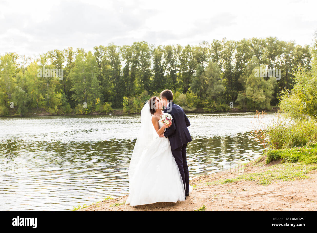Wedding couple standing and kissing near lake Stock Photo - Alamy