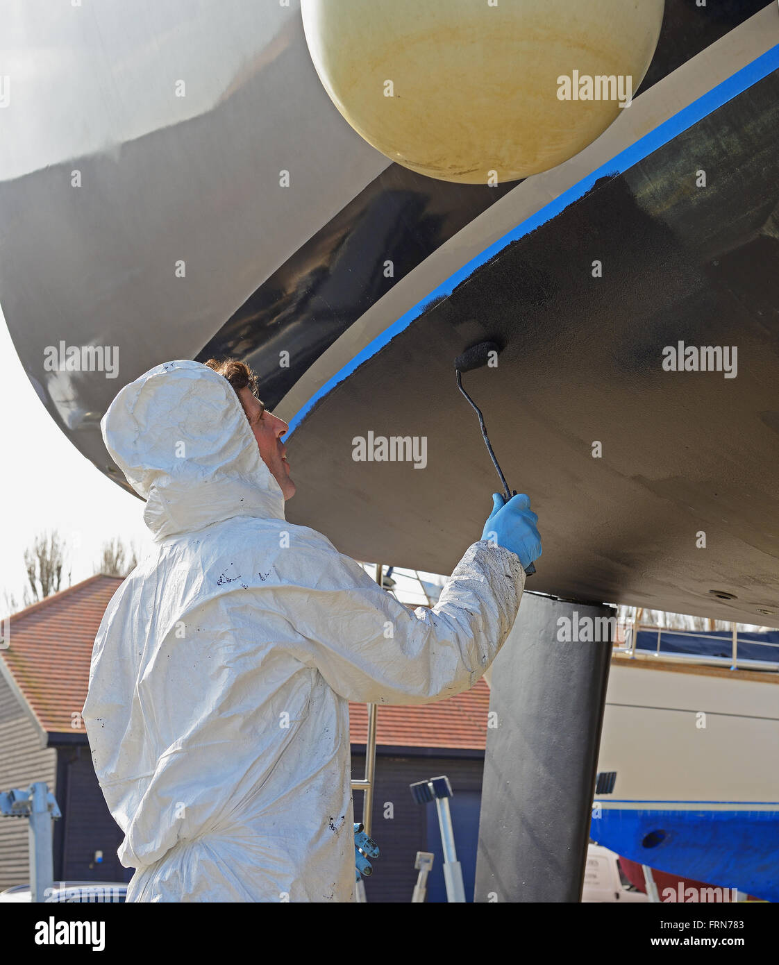 Marina yard worker painting antifouling paint (marine weed preventative by roller on a keeled yacht for the new sailing season. Chichester,West Sussex Stock Photo