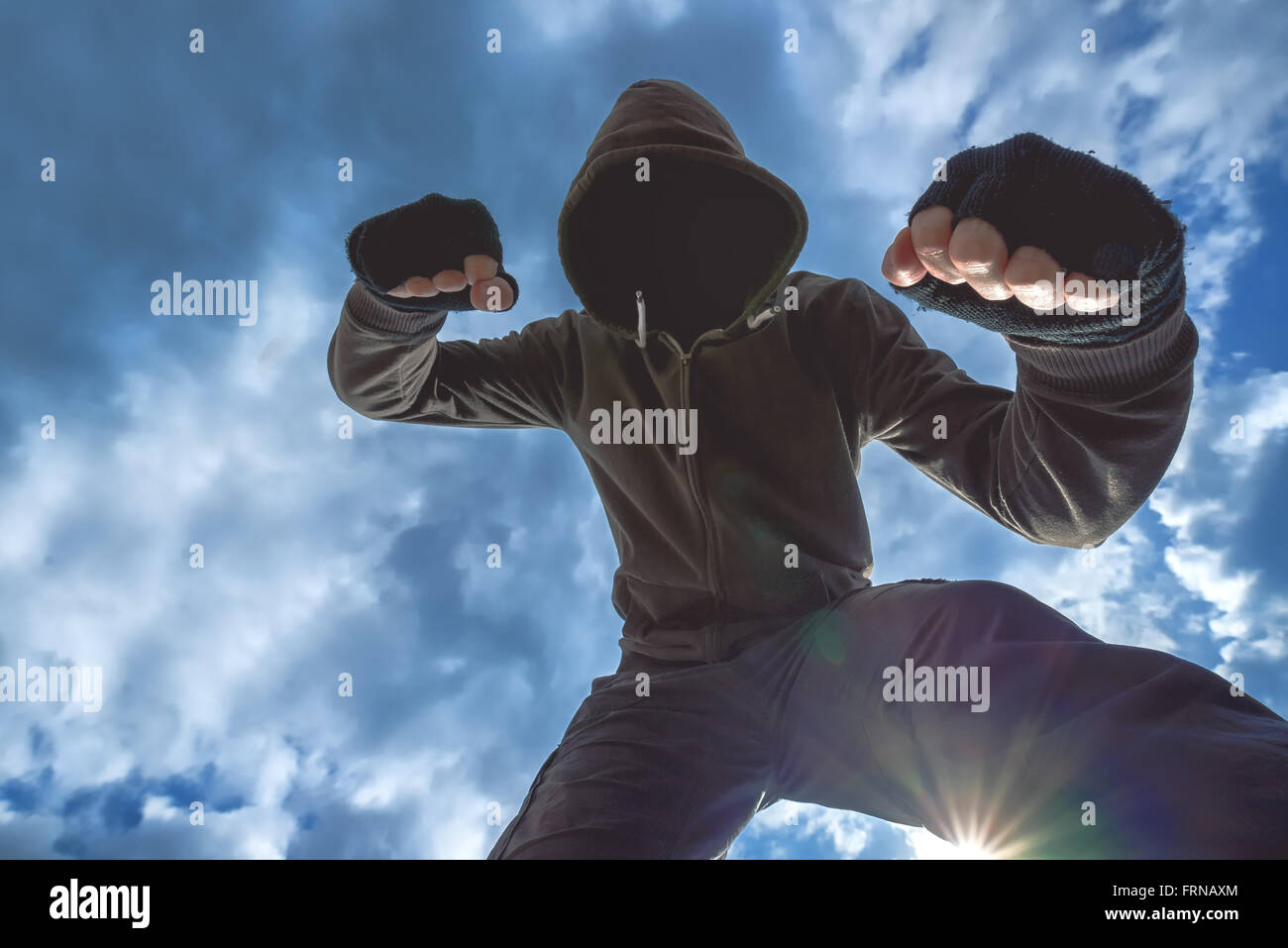 Violent attack, unrecognizable hooded male criminal kicking and punching victim on the street. Stock Photo