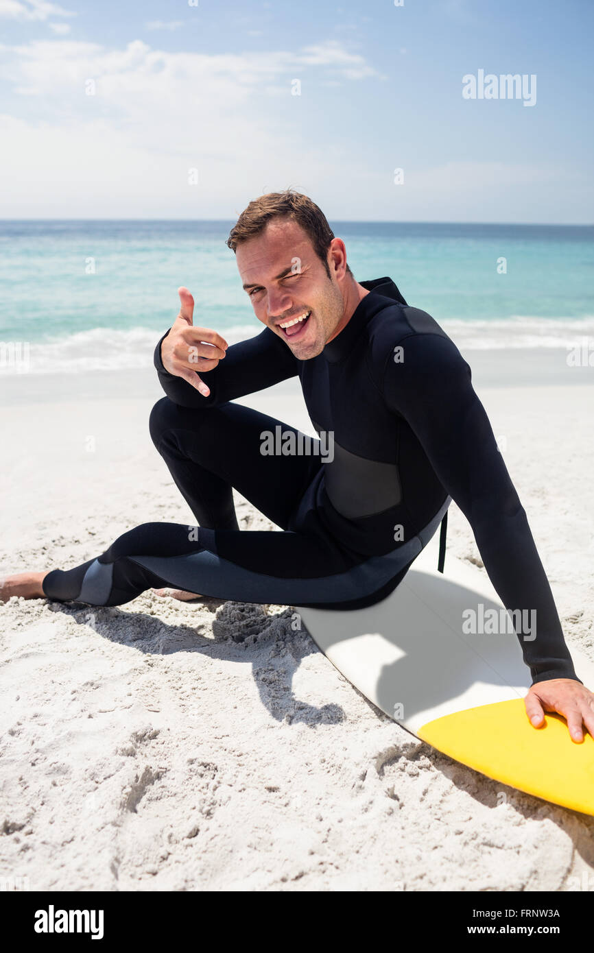 Happy surfer in wetsuit sitting with surfboard on the beach Stock Photo