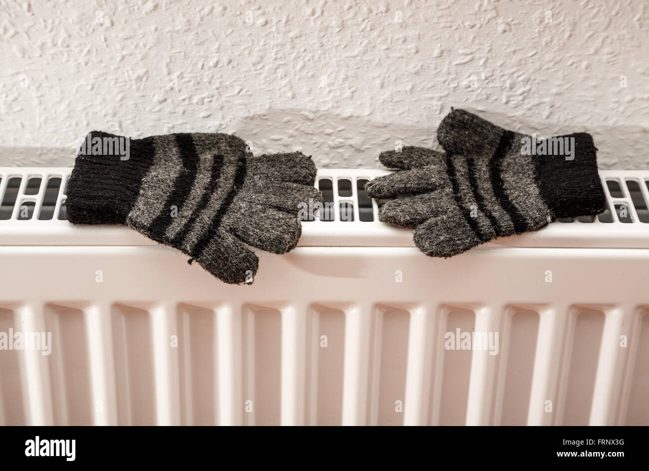 Pair of hand knitted striped woolen gloves drying on an radiator Stock Photo