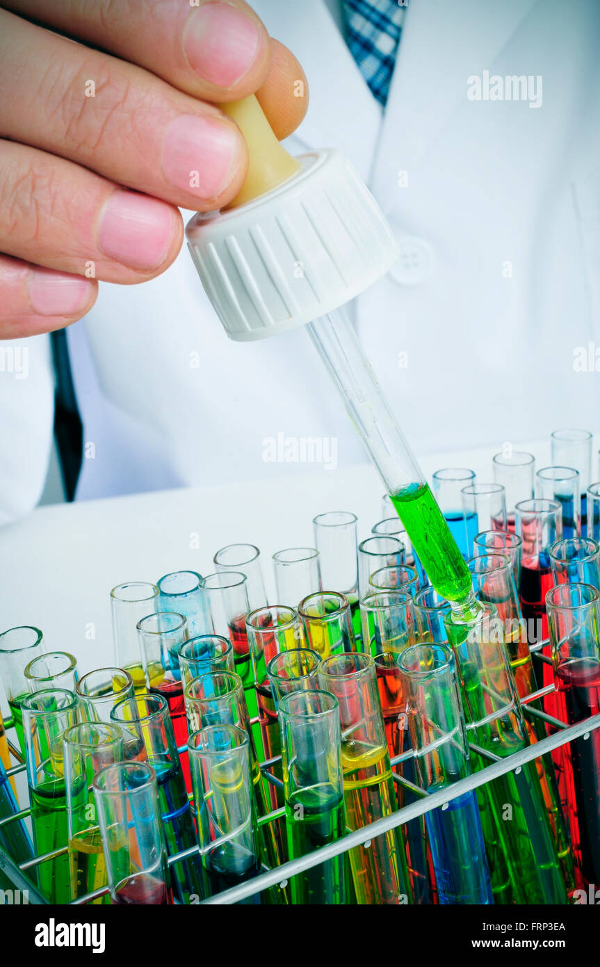 closeup of a young caucasian man in white coat with a dropper in his hand and some test tubes with liquids of different colors i Stock Photo